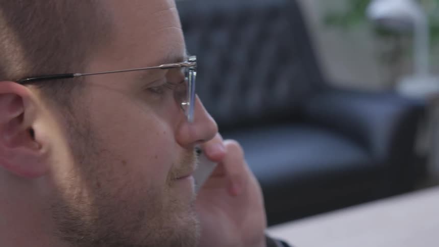A man wearing glasses talks on a cell phone in a living room
