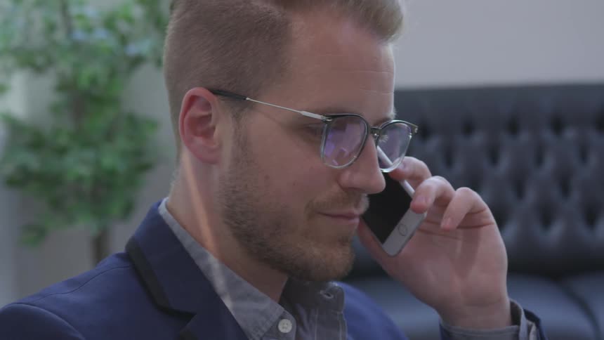 Man with glasses talks on his cell phone and smiles inside an office