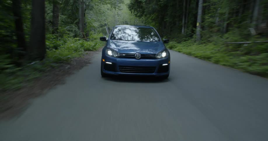 A blue volkswagen travels on a forest road