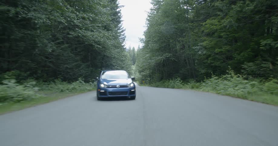 A car driving from one side of the road to the other surrounded by trees