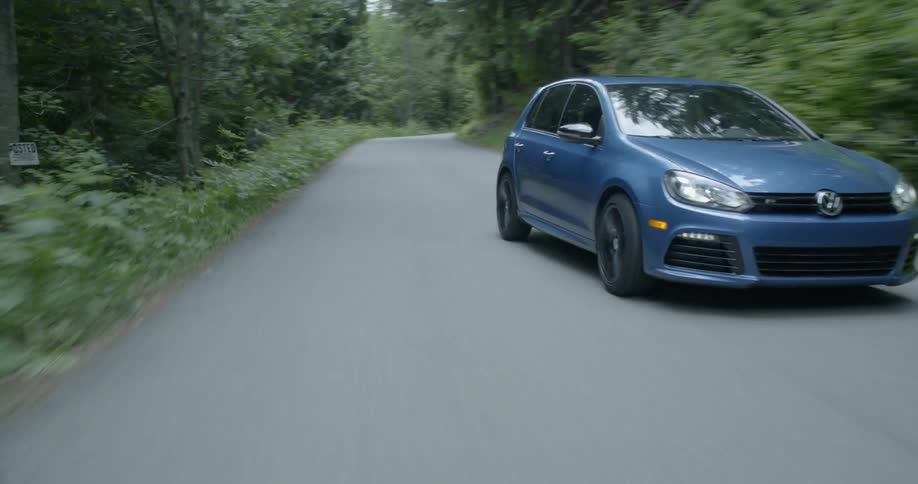 A volkswagen car weaves on a road in the woods at day