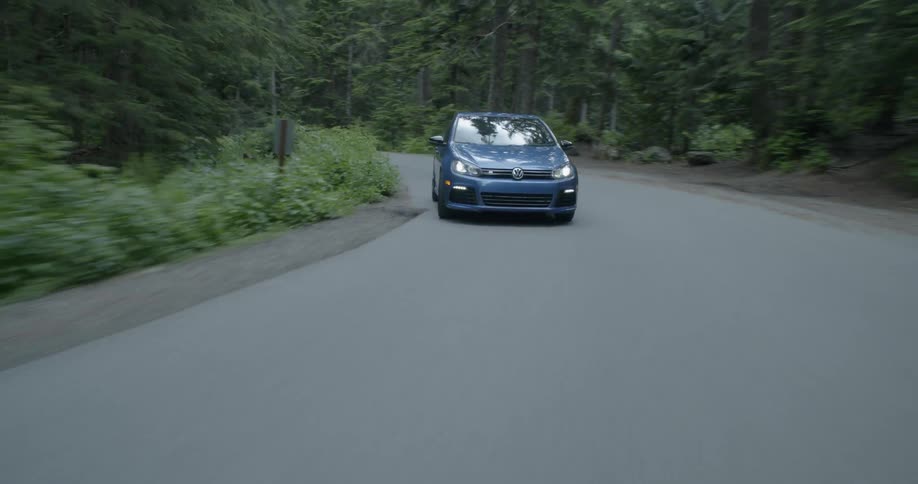 A blue car is driving down the winding road