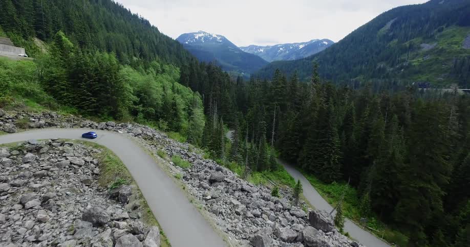 A car driving on a very sharp turned road surrounded by mountains and trees