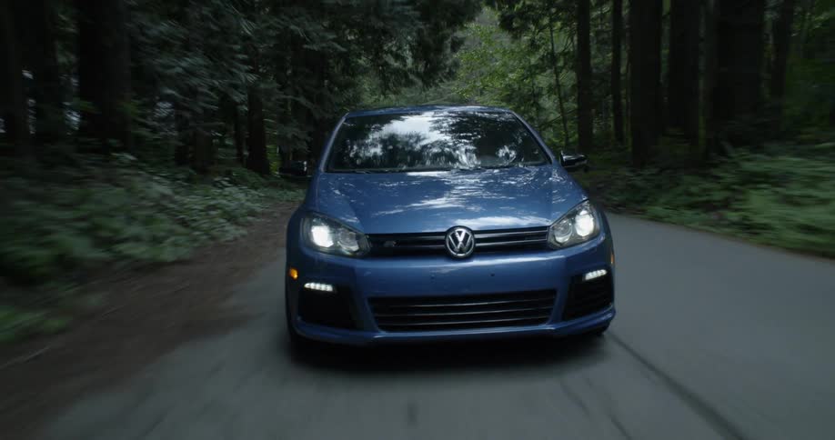 Blue car drives along road in middle of forest