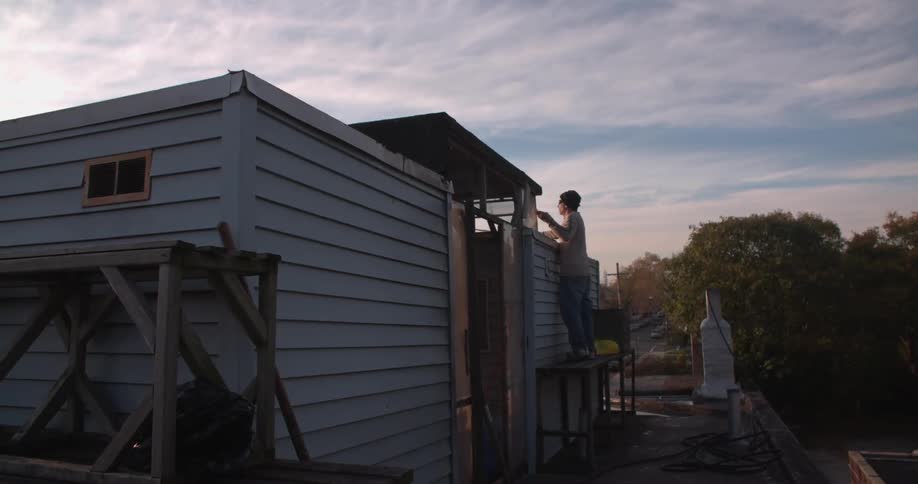 Person stands on scaffolding fixing something on a house roof