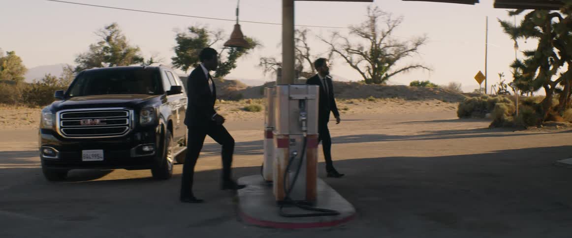 Two men in suits climb out of a black suv and enter a rural gas station