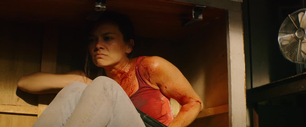 Blood covered woman hiding under a cabinet