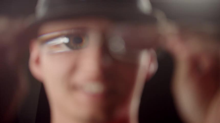 A man holds eyeglasses away from his face which makes his eyes look big