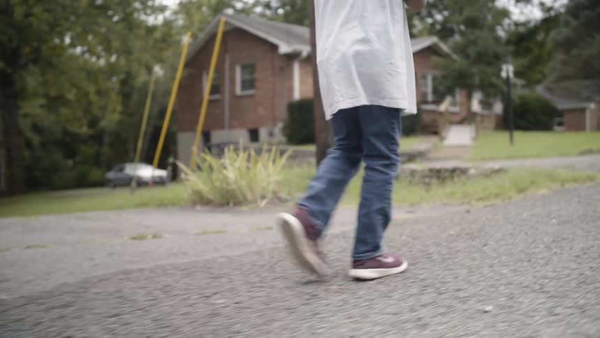 A boy walks on a sidewalk while holding a baseball glove