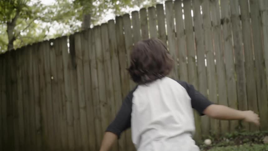 A kid throwing a baseball at a fence