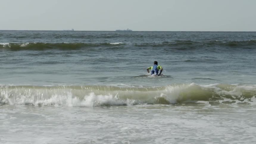 Man with a surfboard heads out into the ocean