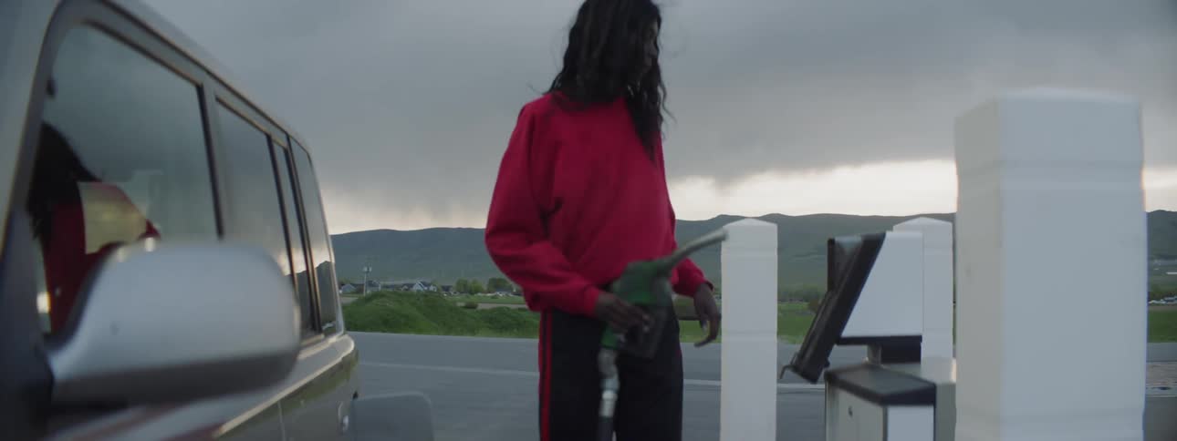 Person pumping gas into a boxy vehicle on a cloudy day
