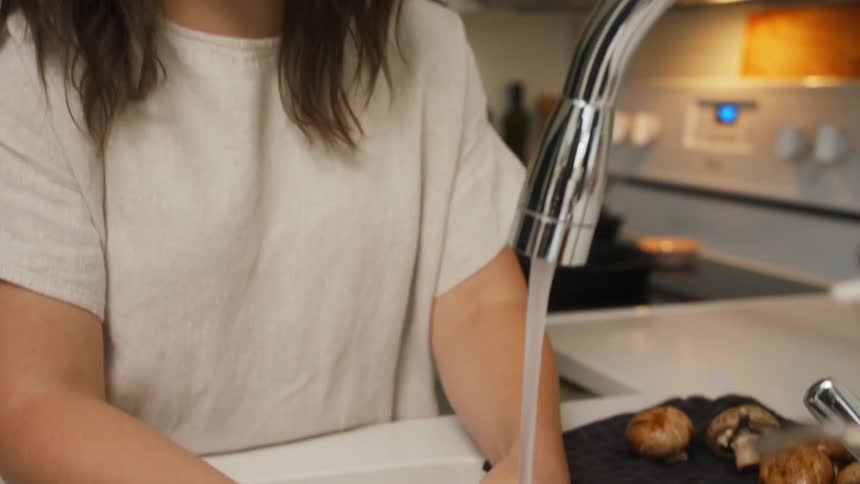 A woman rinsing off mushrooms in the kitchen sink