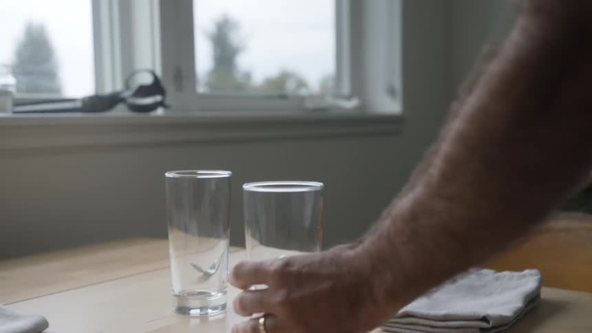 A man puts two glasses on a dining table