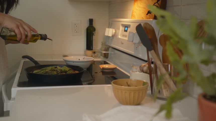 A woman applies olive oil to her dish on the stove in the kitchen