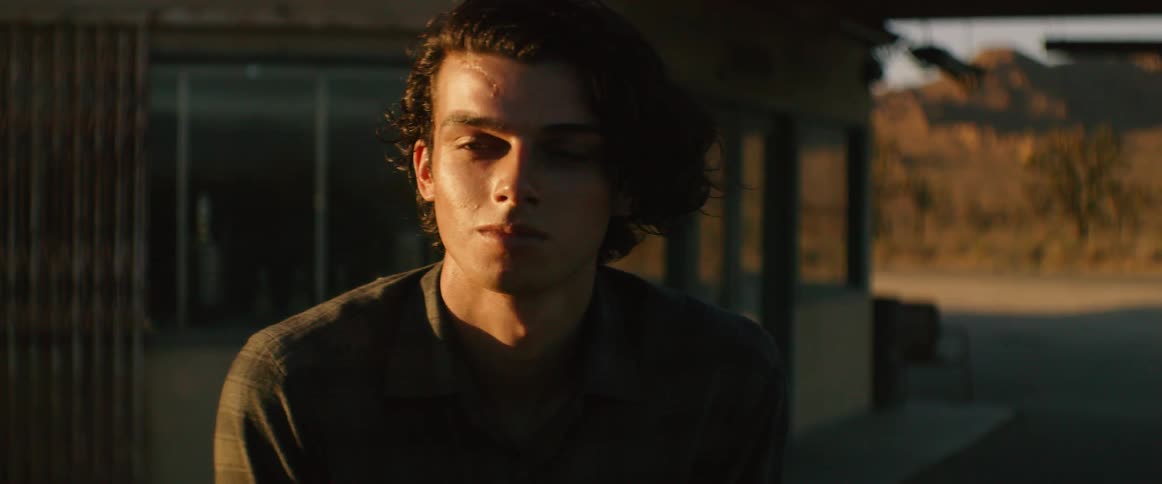 Young man with long hair stand outside building facing sun