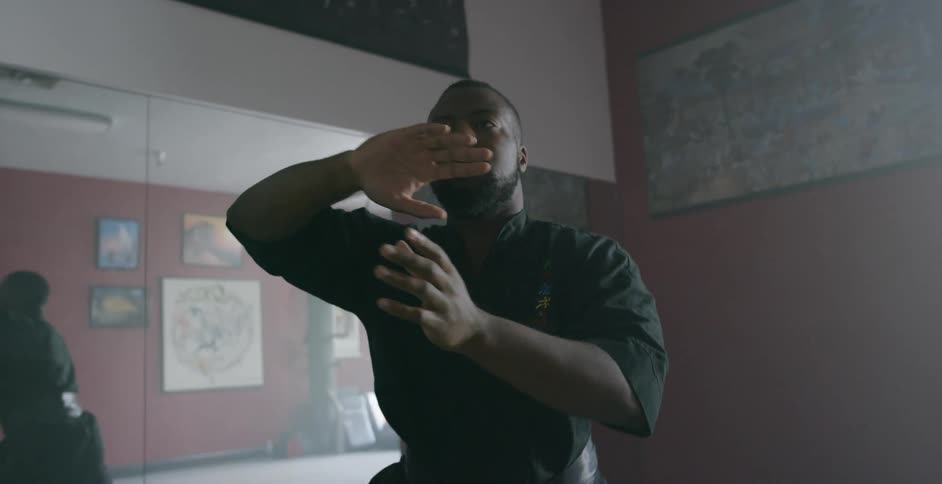 A man stretches and exercises in front of many mirrors on the walls of a dimly lit room