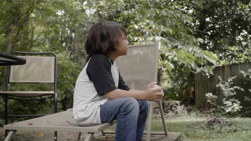 Child is sitting down and holding a baseball