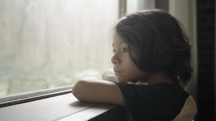 A child leans on the windowsill looking outside