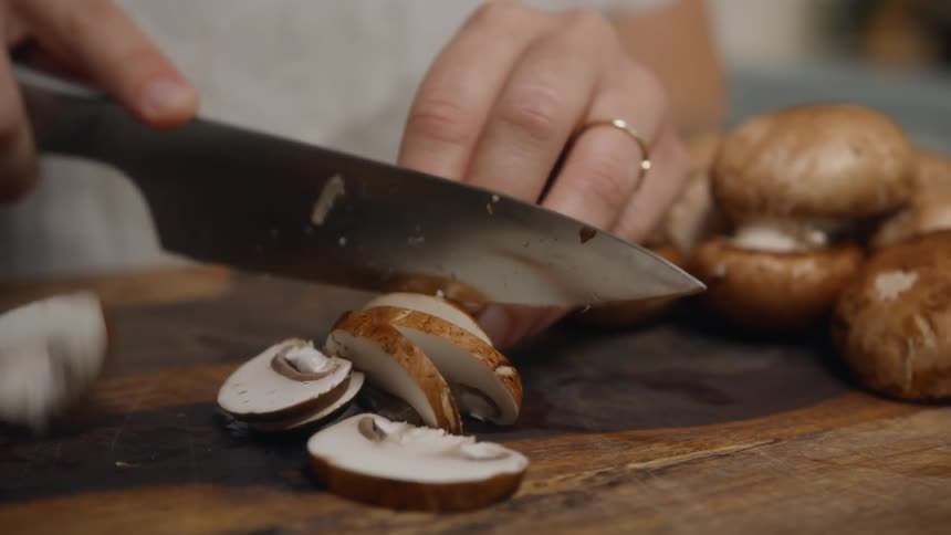 A woman slices mushrooms on a wood cutting board