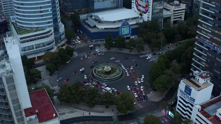 Cars drive around fountain on a city street