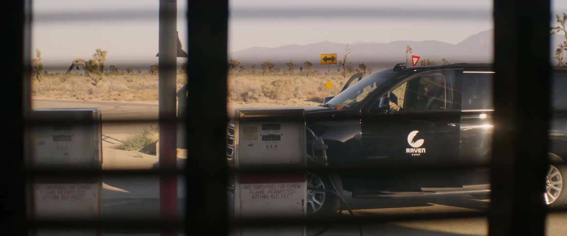A black car is being parked in front of a building and two men wearing black suit get out of the car