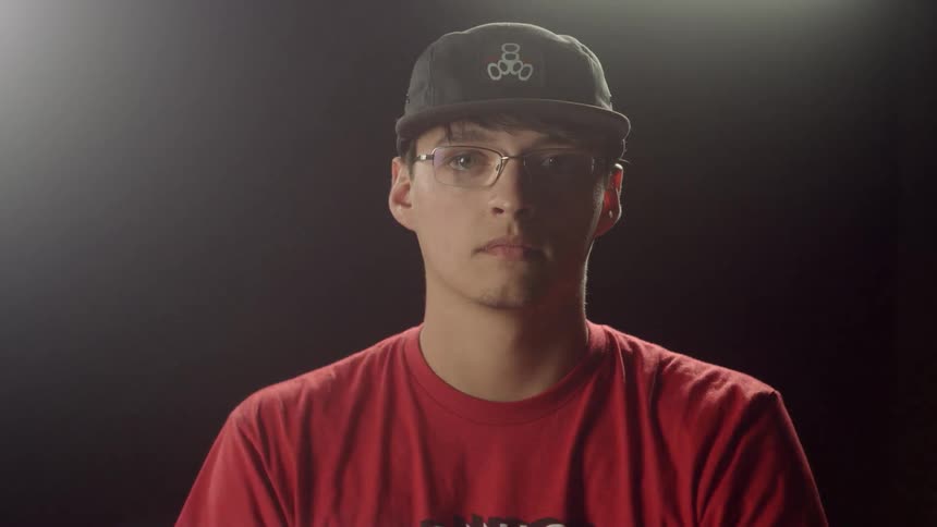 A young man wearing a red shirt and black cap putting on glasses
