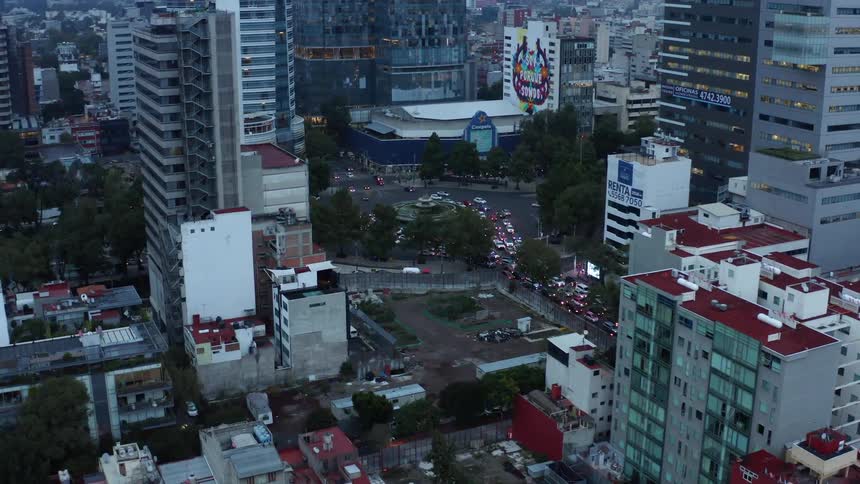 Cars drive in city with tall buildings near dusk