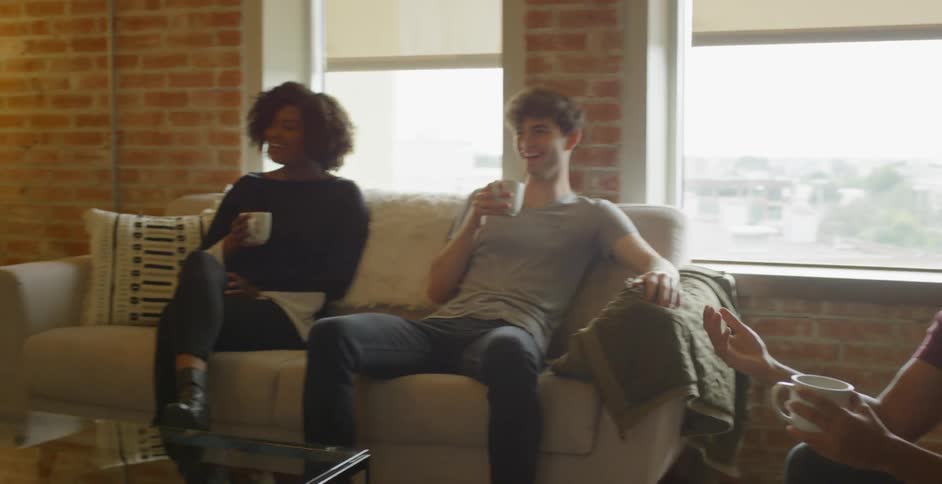 Friends sit in a living room holding coffee mugs