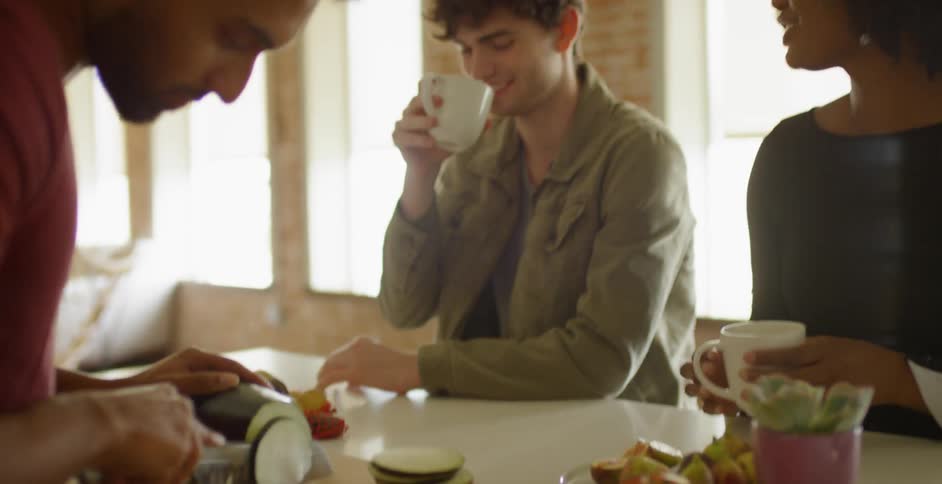 A man slices an eggplant at the counter as friends talk and look on