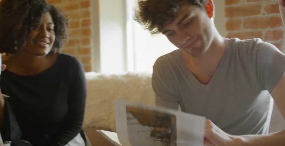 Two men and a woman sit on a couch looking at photographs in a book