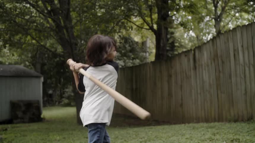 Kid throwing a baseball into the air and swinging their bat at it