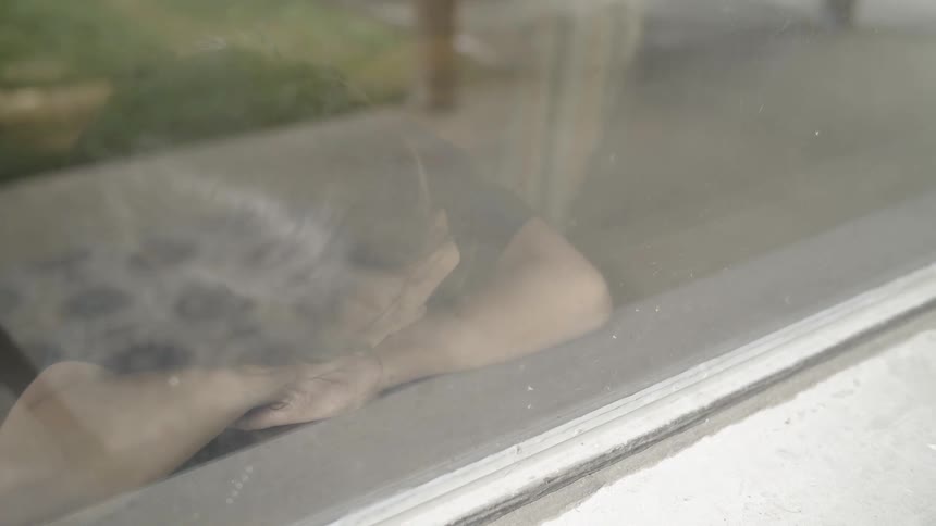 A young child rests their head on a window sill