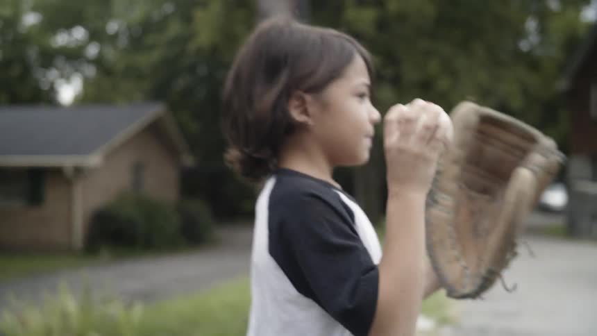 A child tosses a ball into his glove as he walks in a neighborhood