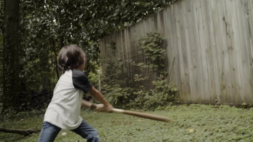 A kid playing baseball in a yard
