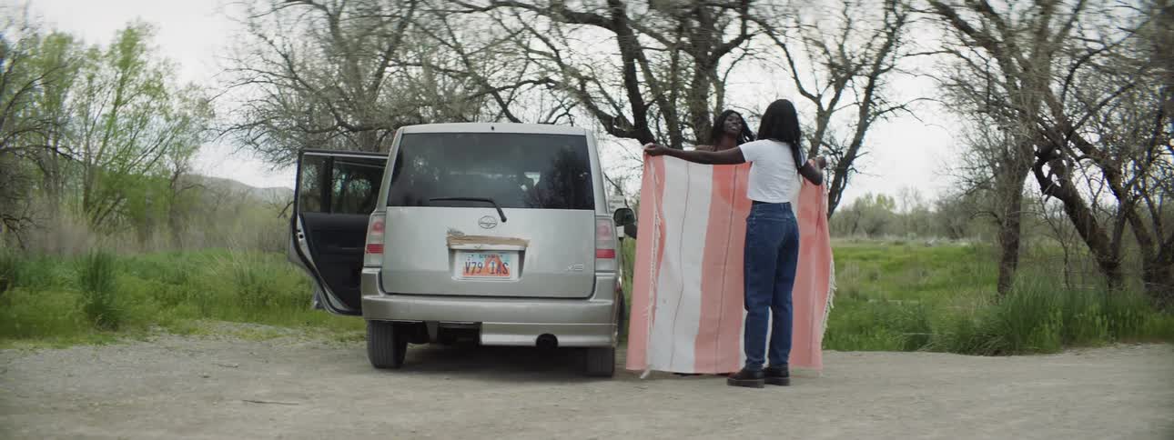 Two women are holding a blanket by a car