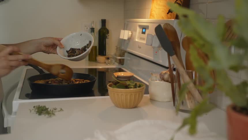 Person scoops food out of bowl into pan on stove