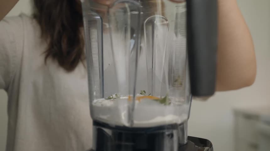 Woman wearing white t shirt cracks an egg into the blender in the kitchen