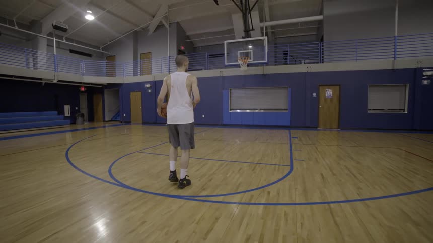Man walks across an indoor basketball court and shoots a basket