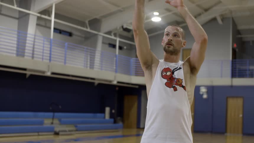 A man stands on a basketball court practicing throws to the basket