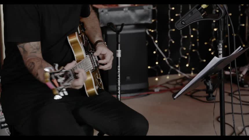 A man with tattooed arms plays guitar on a stage