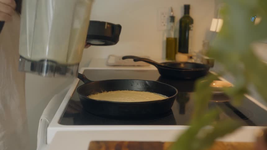 A woman pouring batter into a frying pan in the kitchen
