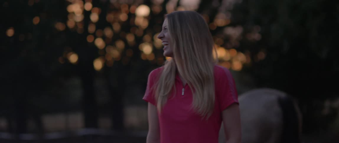 Woman laughing near a horse during sunset