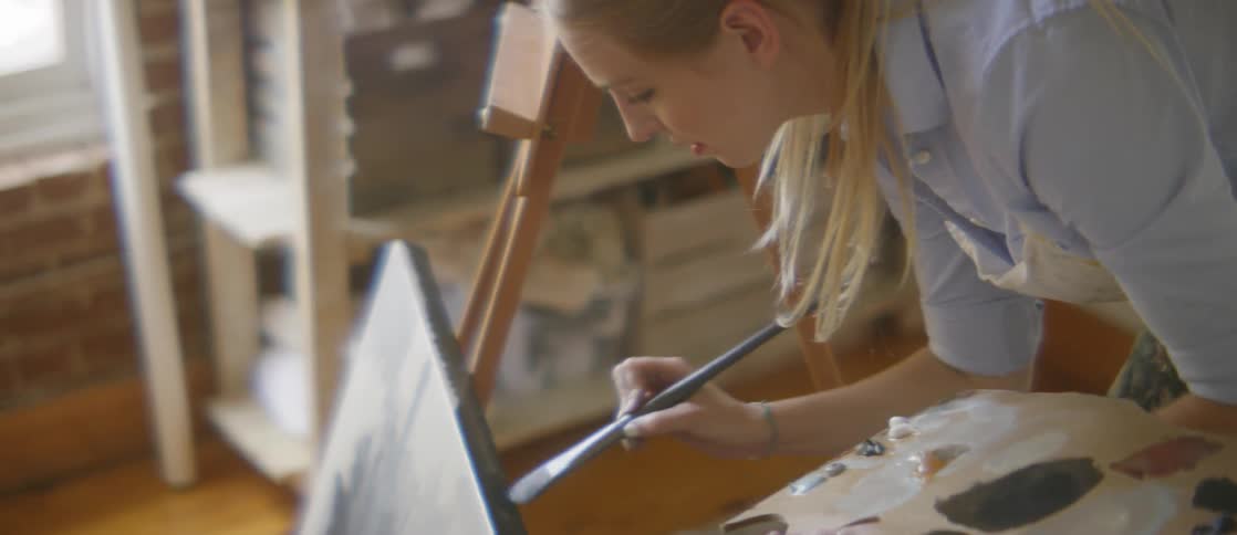 A woman paints the edges of a completed canvas