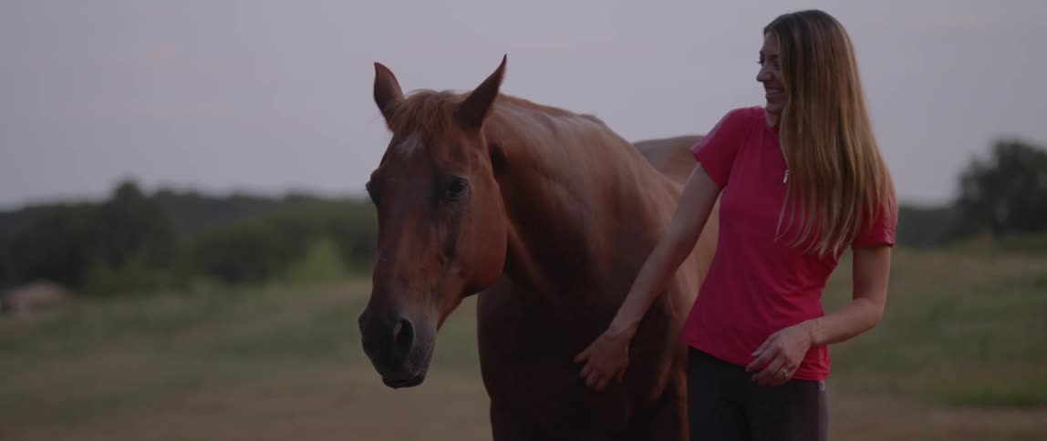 A woman is petting her horse on a windy day