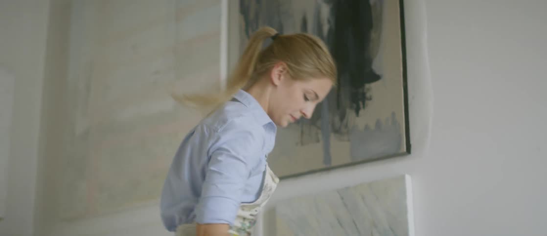 A woman adjusting a painting on the wall