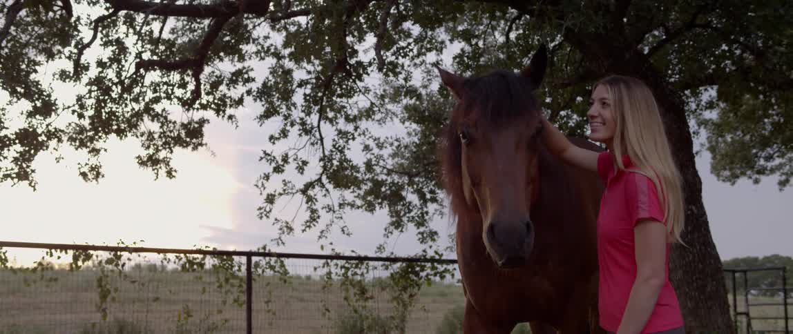 A woman is petting her horse under the tree