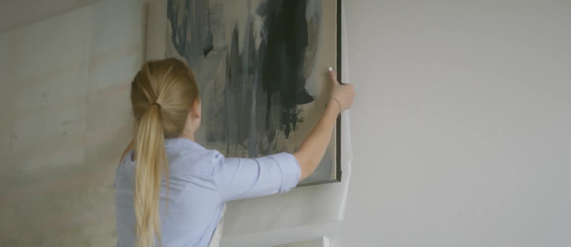 An artist hangs an oil painting on the wall inside her studio