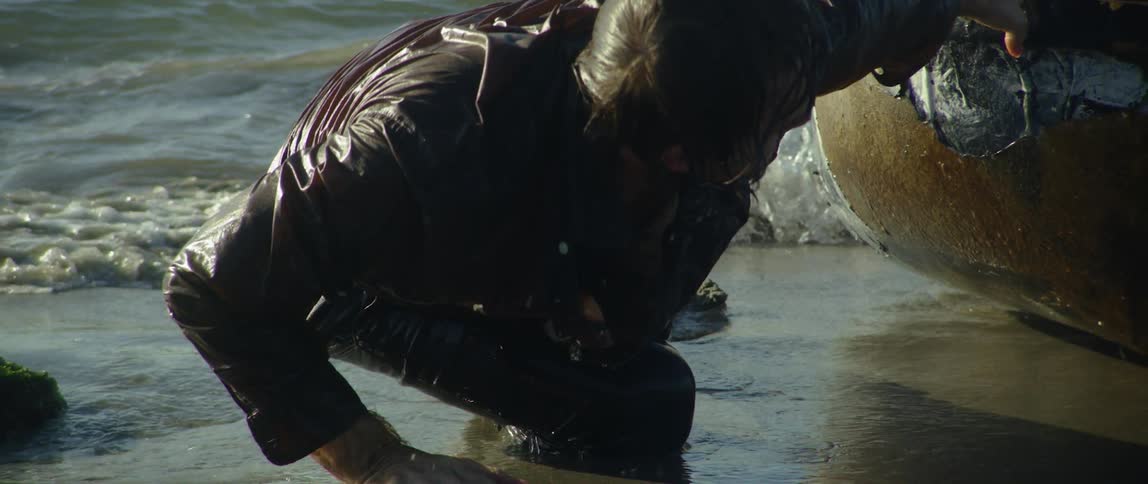 A man crawls on a beach while pulling a boat behind him