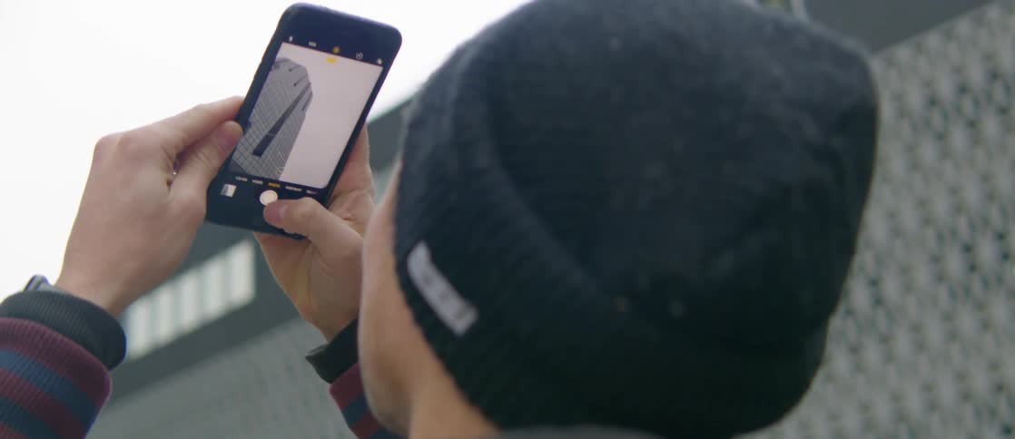A man smiles while taking pictures of a skyscraper